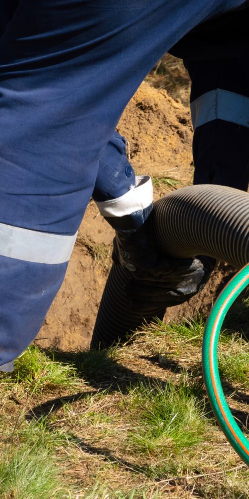 Man worker holding pipe, providing sewer cleaning service outdoor. Sewage pumping machine is unclogging blocked manhole